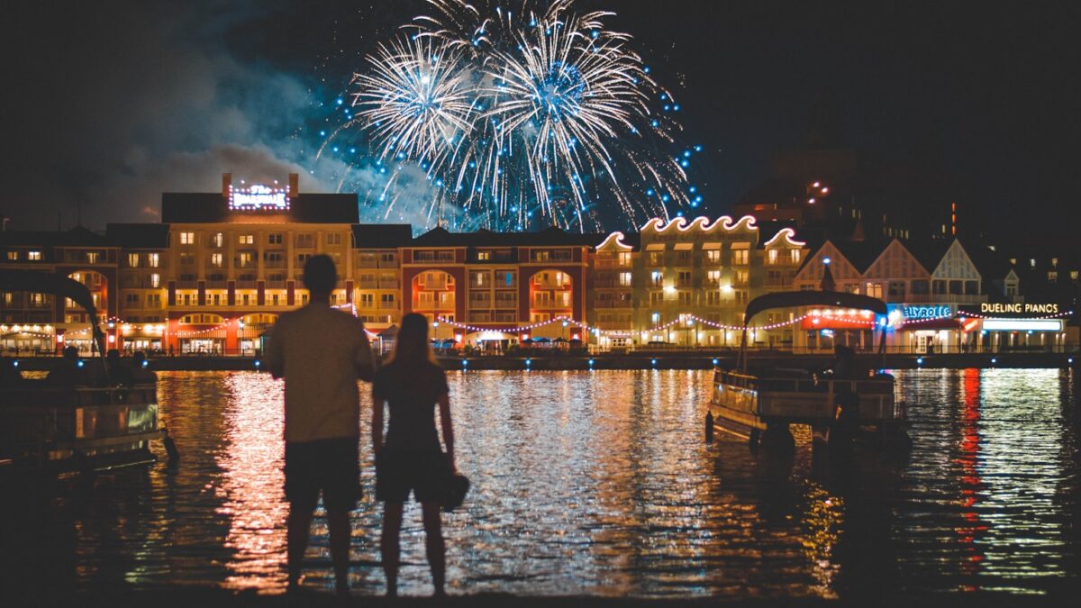 two people standing beside body of water watching fireworks